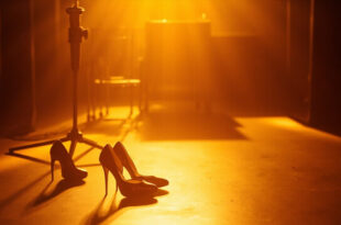 High heeled shoes next to vintage microphone in retro television studio setting with warm amber lighting