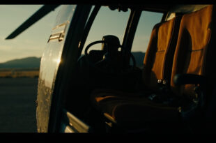 Empty helicopter seat with unbuckled safety harness against overcast Montana sky at dusk.