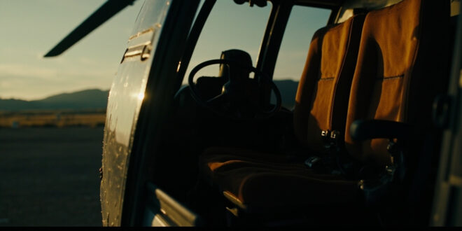 Empty helicopter seat with unbuckled safety harness against overcast Montana sky at dusk.