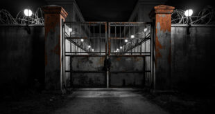 Heavy metal prison gates partially open showing concrete walls and security barriers in overcast lighting