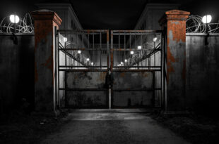 Heavy metal prison gates partially open showing concrete walls and security barriers in overcast lighting