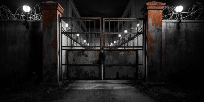 Heavy metal prison gates partially open showing concrete walls and security barriers in overcast lighting