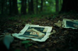 Scattered modeling photographs and papers abandoned in dark forest debris near highway