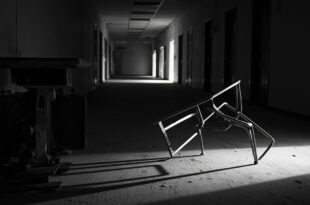Overturned metal chair in empty school hallway with fluorescent lights and closed doors