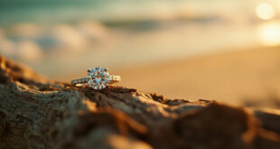 Diamond engagement ring with round-cut stone and diamond band resting on driftwood against ocean waves