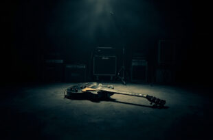 Vintage Gibson Les Paul guitar under single spotlight on empty dark concert stage with amplifiers in shadows