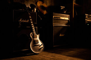 Electric guitar leaning against amplifier in dark studio with vinyl records scattered on floor
