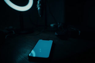 Dark smartphone on wooden desk beside silent microphone and dimmed ring light in shadowy room