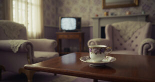 Fine bone china teacup on saucer sits beside vintage television in traditional English parlor with floral wallpaper