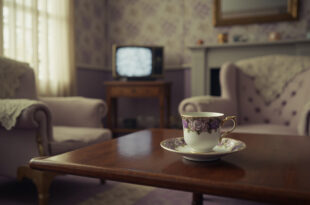 Fine bone china teacup on saucer sits beside vintage television in traditional English parlor with floral wallpaper