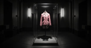 Pink 1960s suit jacket displayed in glass museum case under focused lighting in archival storage vault