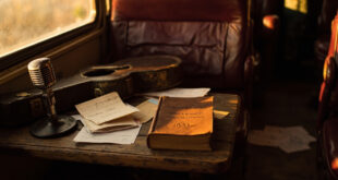 Leather book on wooden surface with vintage microphone, guitar case, and handwritten notes in warm amber lighting