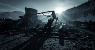 Burned structural framework of multi-story building stands against winter mountain backdrop with dark sky
