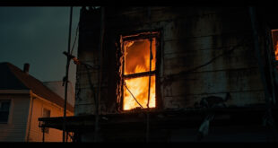Burned house exterior with damaged upper window frame and exposed interior structure after intense nighttime fire