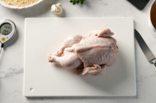 Raw chicken on white cutting board with meat thermometer and kitchen knife on clean counter surface